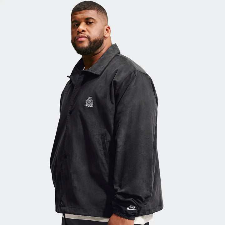 Men's Nike Club black corduroy coaches jacket modeled from the front, showing the embroidered logo and Nike cuff detail.