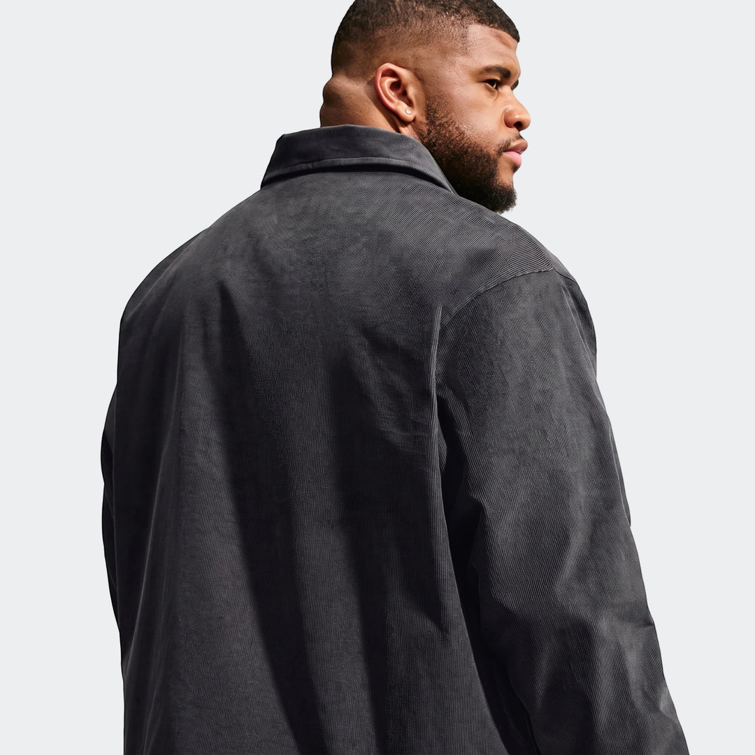 Back view of a man wearing a dark grey Nike Club Men's Corduroy Coaches Jacket, showcasing the ribbed texture and collar.