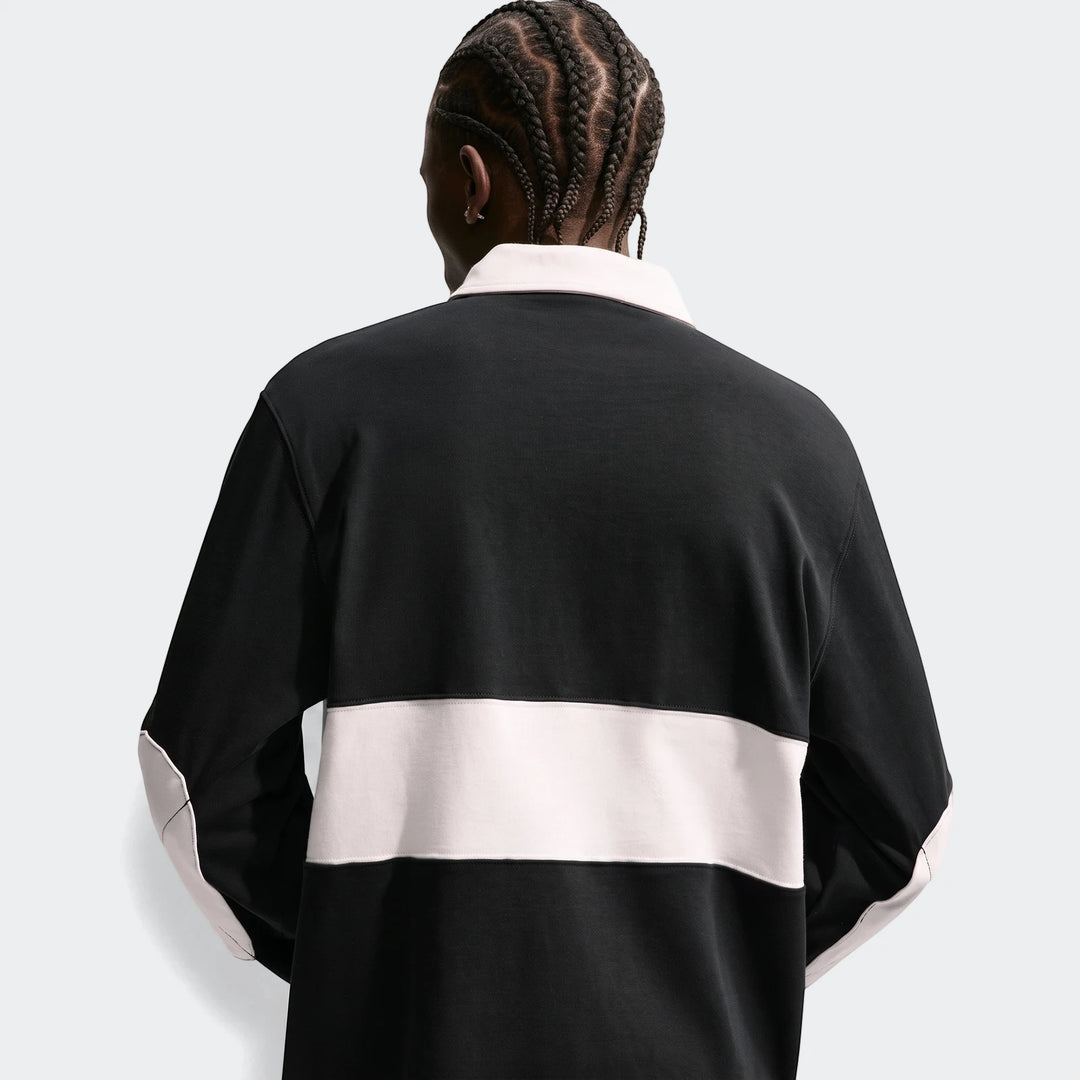 Rear view of a man wearing a black Nike Club Men's Long-Sleeve Rugby Top with a light pink collar and a horizontal stripe.
