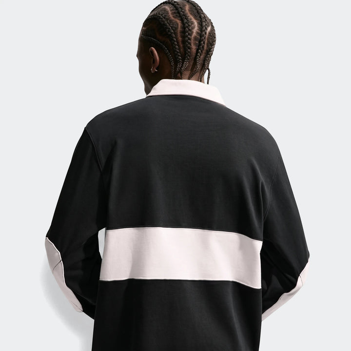 Rear view of a man wearing a black Nike Club Men's Long-Sleeve Rugby Top with a light pink collar and a horizontal stripe.