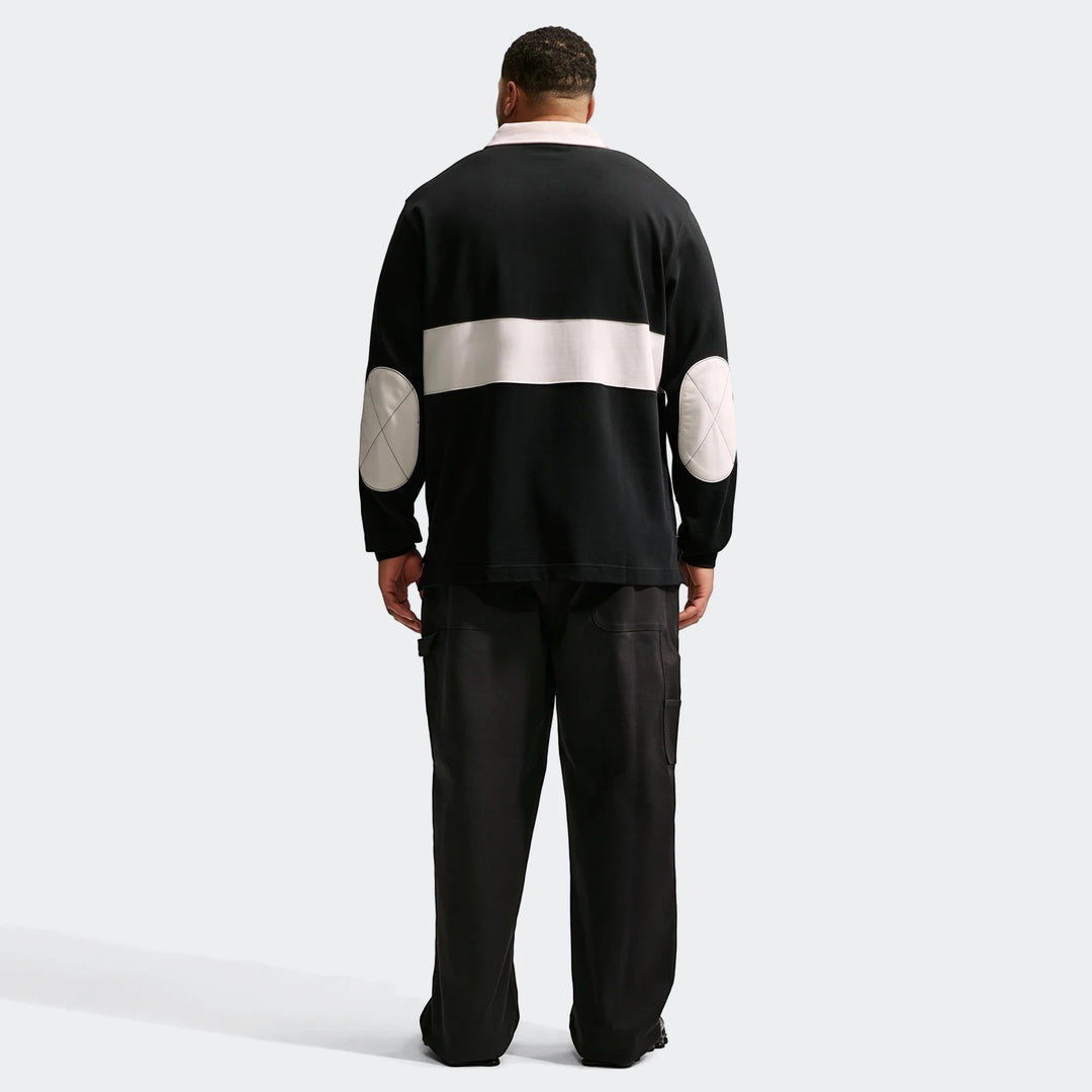 Rear view of a men's Nike Club long-sleeve rugby top in black with a light-colored stripe and elbow patches, paired with