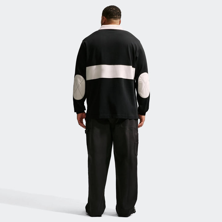 Rear view of a men's Nike Club long-sleeve rugby top in black with a light-colored stripe and elbow patches, paired with