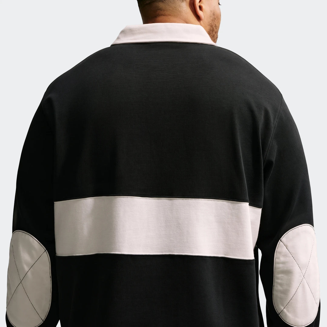Men's long-sleeve rugby top from Nike Club in black with off-white collar, back stripe, and elbow patches, shown from the