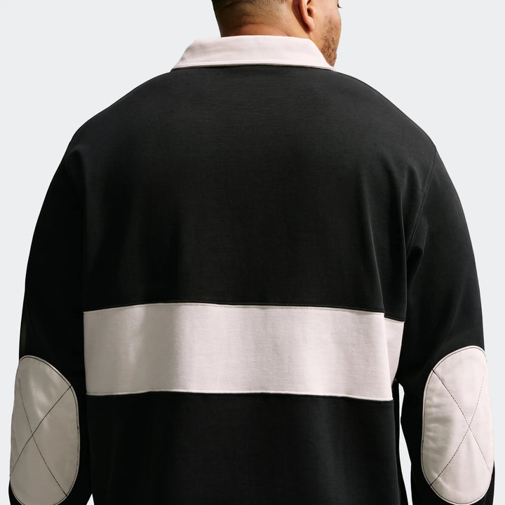 Men's long-sleeve rugby top from Nike Club in black with off-white collar, back stripe, and elbow patches, shown from the