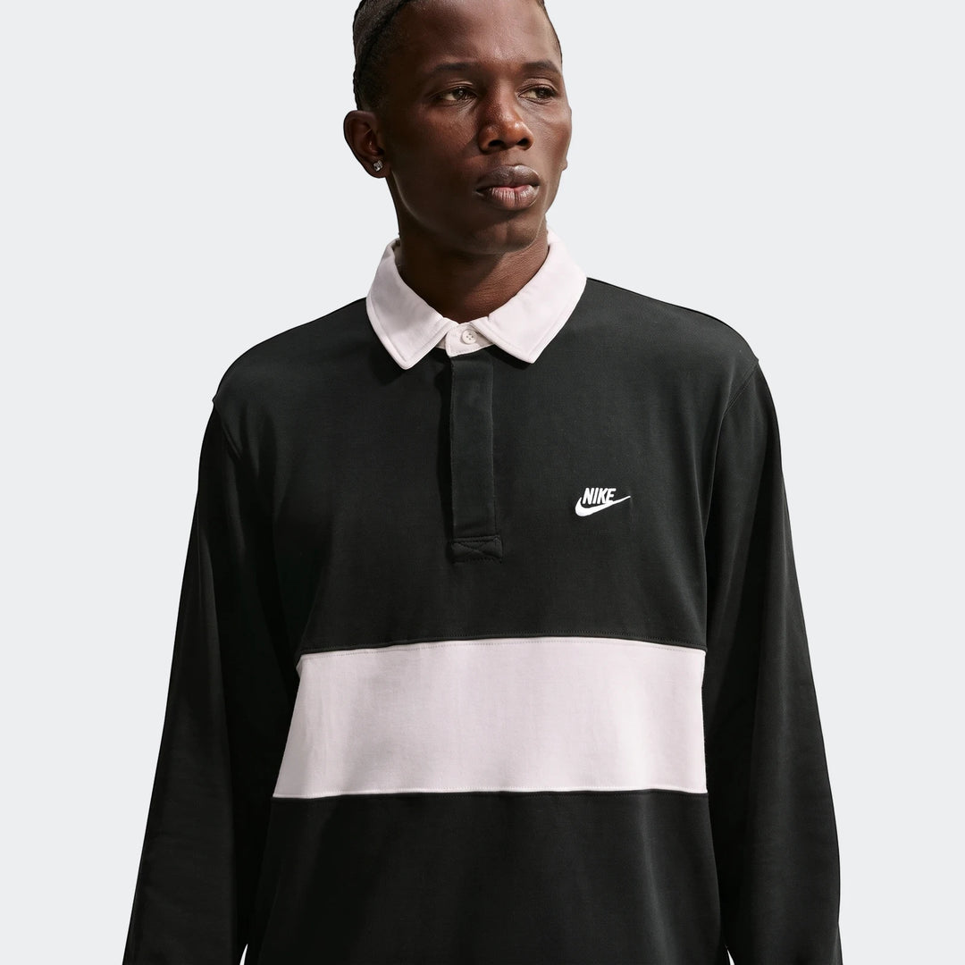 Male model wearing a Nike Club Men's Long-Sleeve Rugby Top in black with a light pink horizontal stripe and white collar.