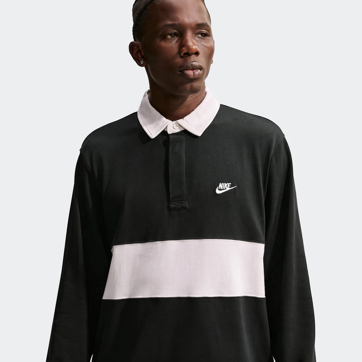 Male model wearing a Nike Club Men's Long-Sleeve Rugby Top in black with a light pink horizontal stripe and white collar.