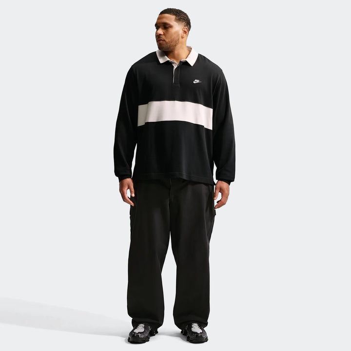Nike Club Men's Long-Sleeve Rugby Top in black with a white stripe, worn by a man, full body view.