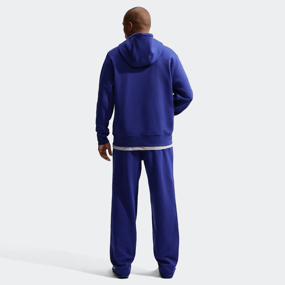 Back view of a man wearing a blue Nike Club men's pullover fleece hoodie and matching blue sweatpants, standing.