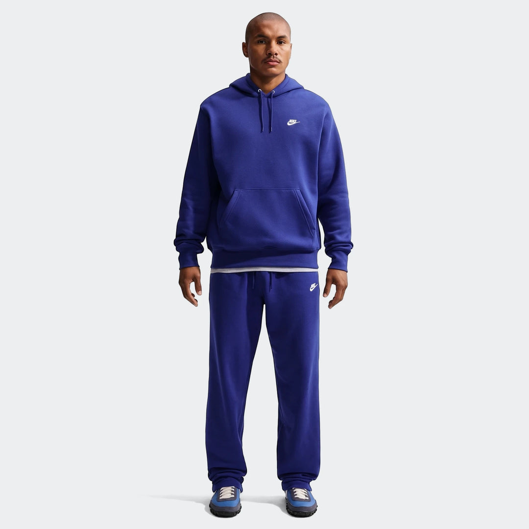 A man models a blue Nike Club Pullover Fleece Hoodie with matching sweatpants, showcasing the full outfit.