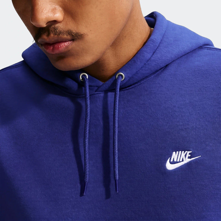 Close-up of a man wearing a royal blue Nike Club Men's Pullover Fleece Hoodie, featuring a white Nike logo on the chest.