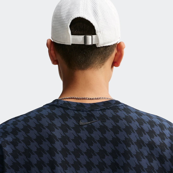 Back view of a person wearing a white Nike Club Rules T-Shirt, a white baseball cap, and a silver chain necklace.