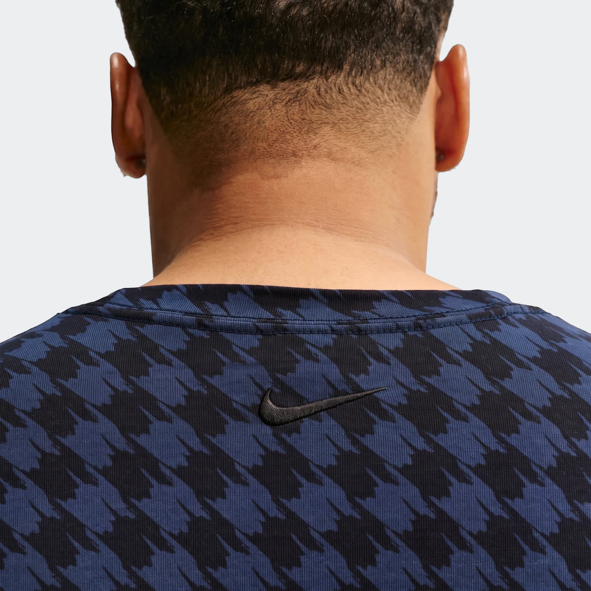 Back view of a person wearing a Nike Club Rules T-Shirt in blue and black houndstooth pattern.