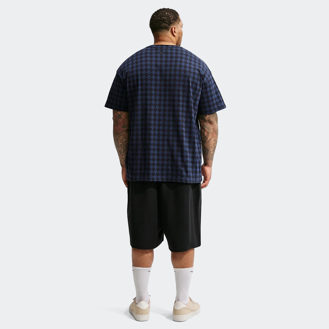 Men's Nike Club Rules t-shirt in blue and black houndstooth pattern, shown from the back with shorts and sneakers.