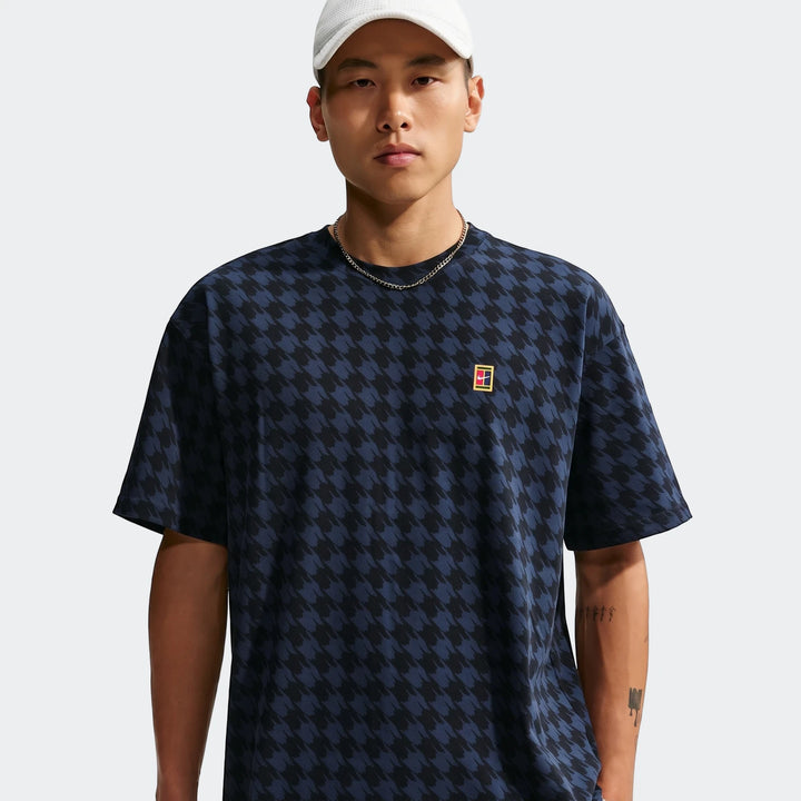 Male model wearing a Nike Club Rules t-shirt with a black and navy houndstooth pattern and a small tennis logo.