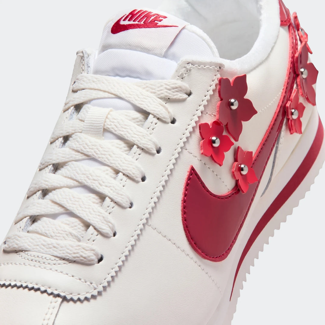 Close-up of a white Nike Cortez Leather Women's Shoe with a red Nike swoosh and red floral appliqués with silver studs.