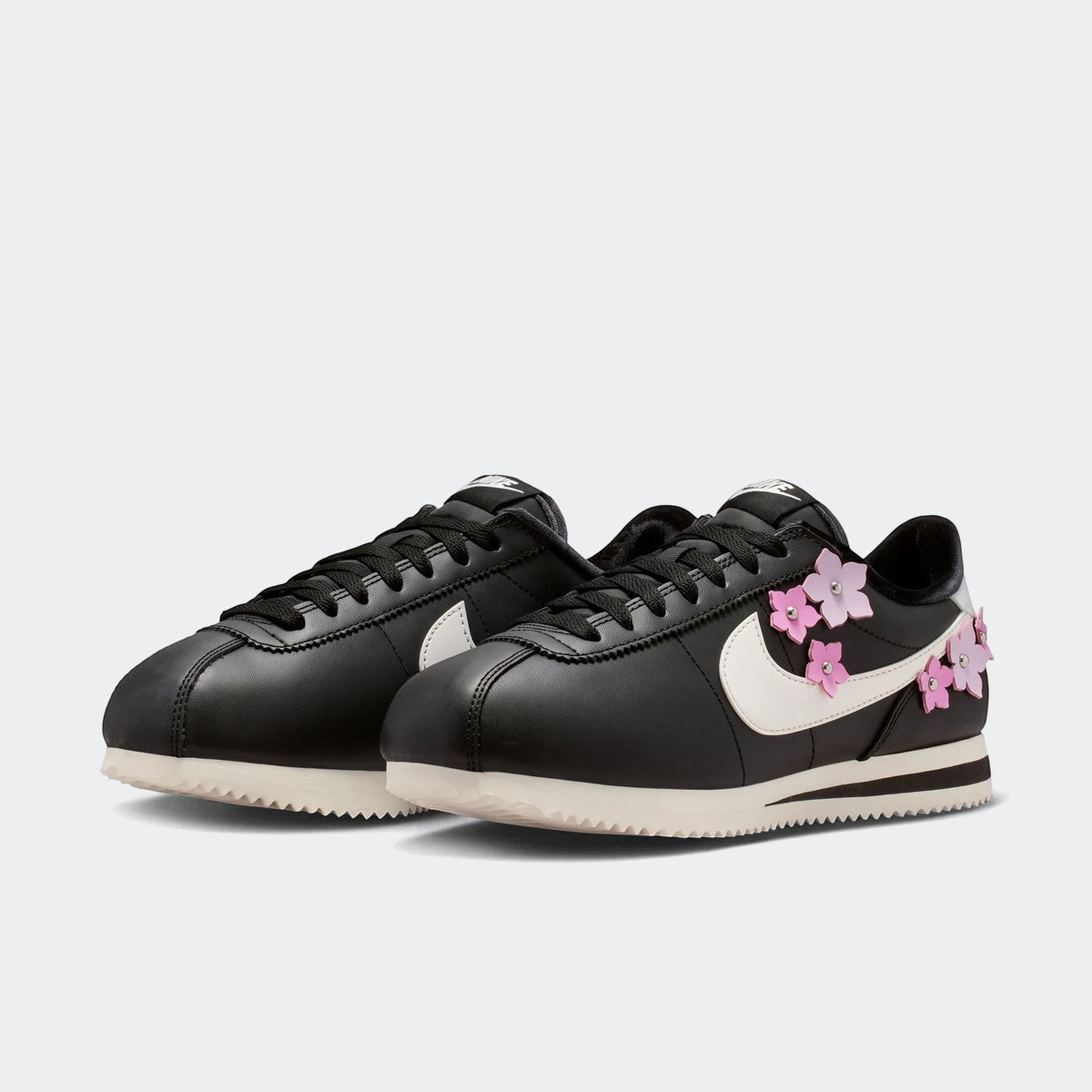 Pair of black Nike Cortez Leather Women's Shoes featuring a white swoosh and vibrant pink floral embellishments.