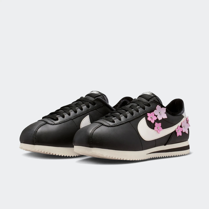 Pair of black Nike Cortez Leather Women's Shoes featuring a white swoosh and vibrant pink floral embellishments.