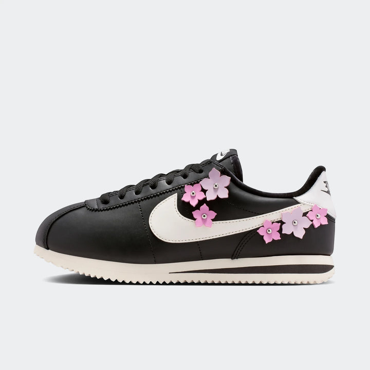 Black Nike Cortez Leather Women's Shoes with pink cherry blossom flower embellishments and a white swoosh, shown in a side