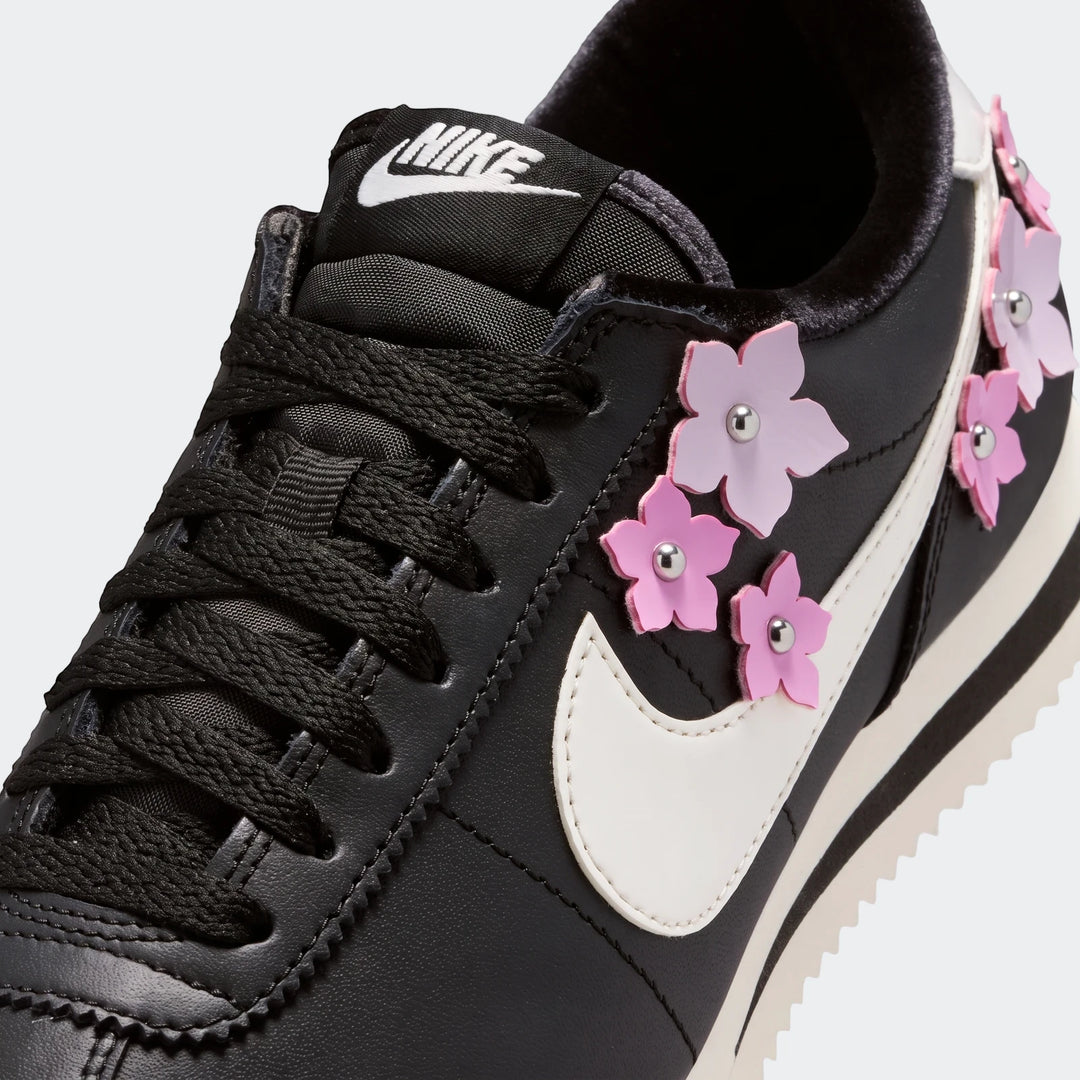 Nike Cortez Leather Women's Shoes in black, featuring a white swoosh and pink floral embellishments, shown in a close-up.
