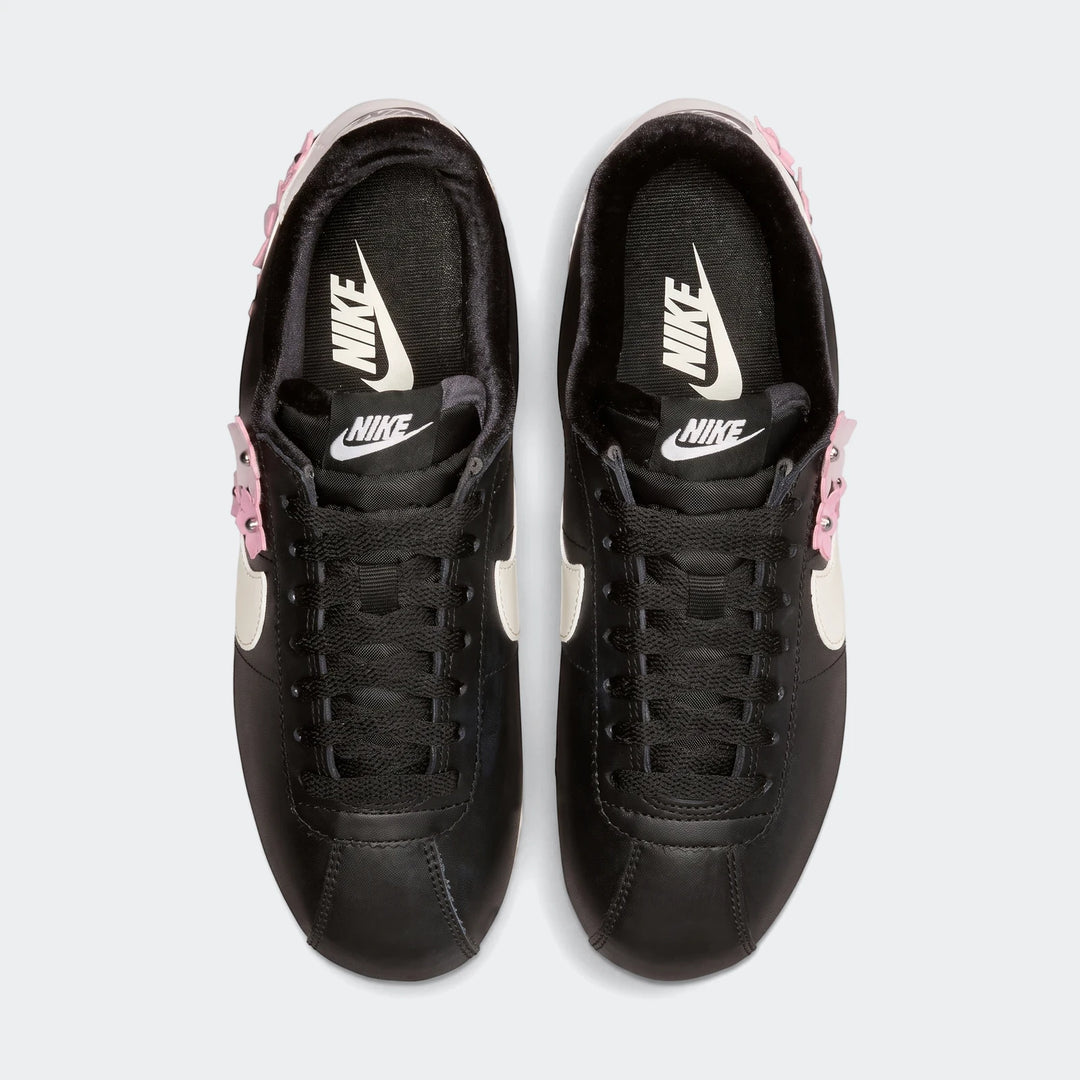 Top-down view of black Nike Cortez Leather Women's Shoes featuring white swooshes and pink studded accents on a white