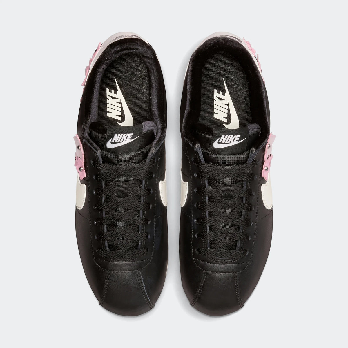 Top-down view of black Nike Cortez Leather Women's Shoes featuring white swooshes and pink studded accents on a white