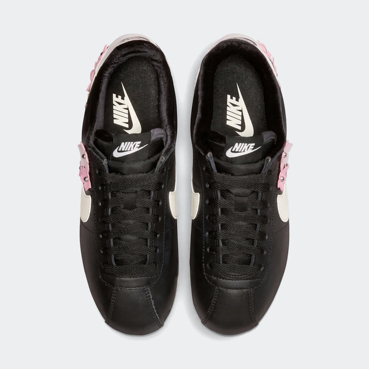 Top-down view of black Nike Cortez Leather Women's Shoes featuring white swooshes and pink studded accents on a white