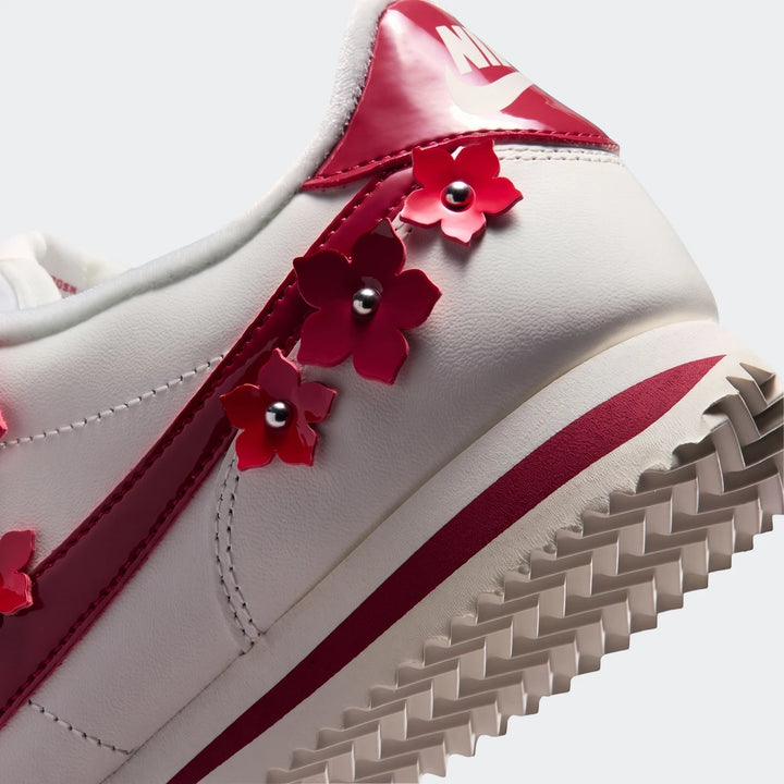 Close-up of the heel and side of a white Nike Cortez Leather Women's shoe with red accents and flower embellishments.