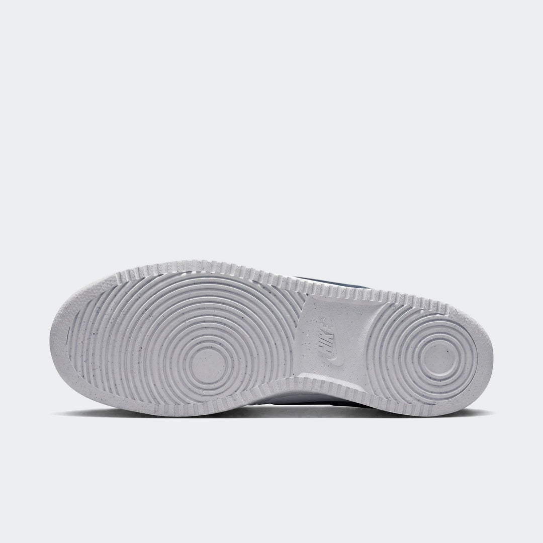 Bottom view of white Nike Court Vision Low men's shoes, showcasing the durable rubber outsole with speckled texture and