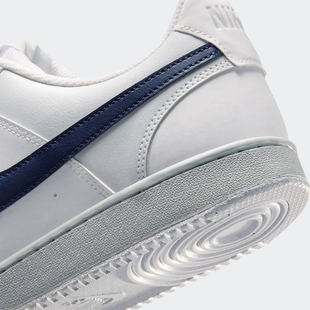 White Nike Court Vision Low men's shoes with a navy blue swoosh stripe, viewed from the rear-side, highlighting the heel and