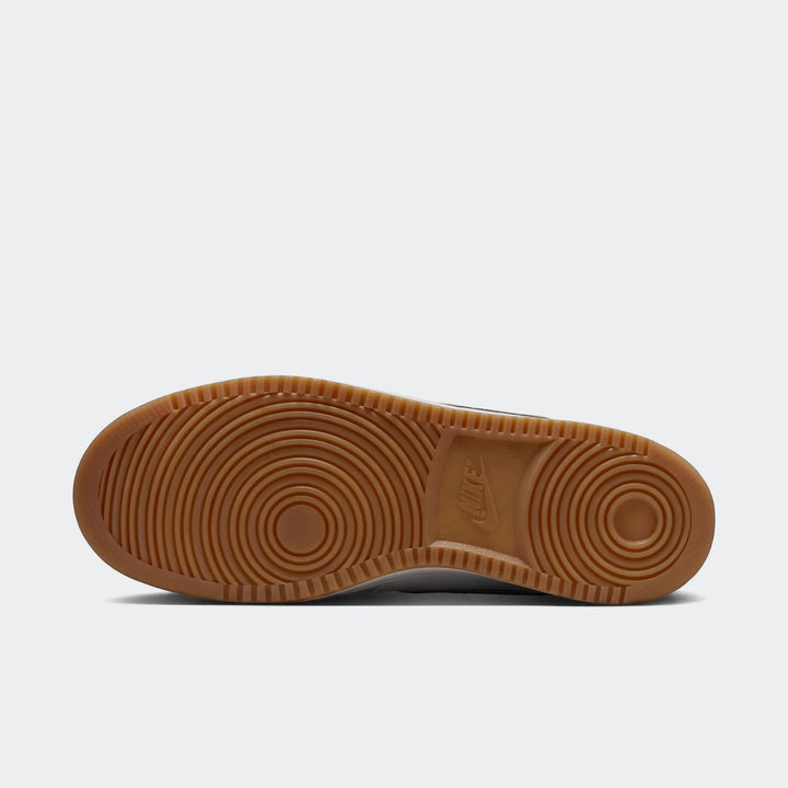 Bottom view of a Nike Court Vision Low men's shoe, showcasing the brown gum sole with circular traction pattern and white