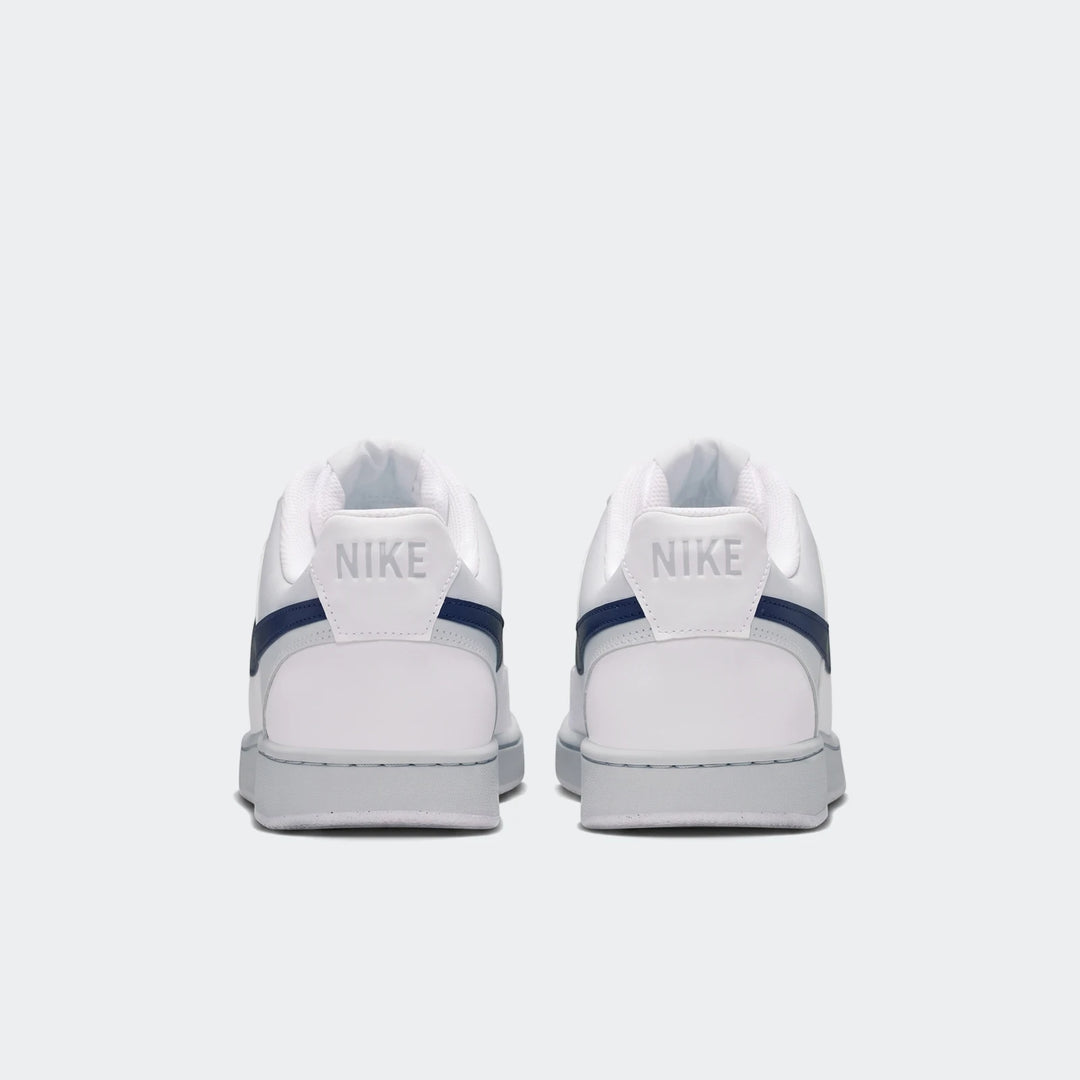 Rear view of two white Nike Court Vision Low men's shoes with navy blue accents and grey soles, displayed on a clean