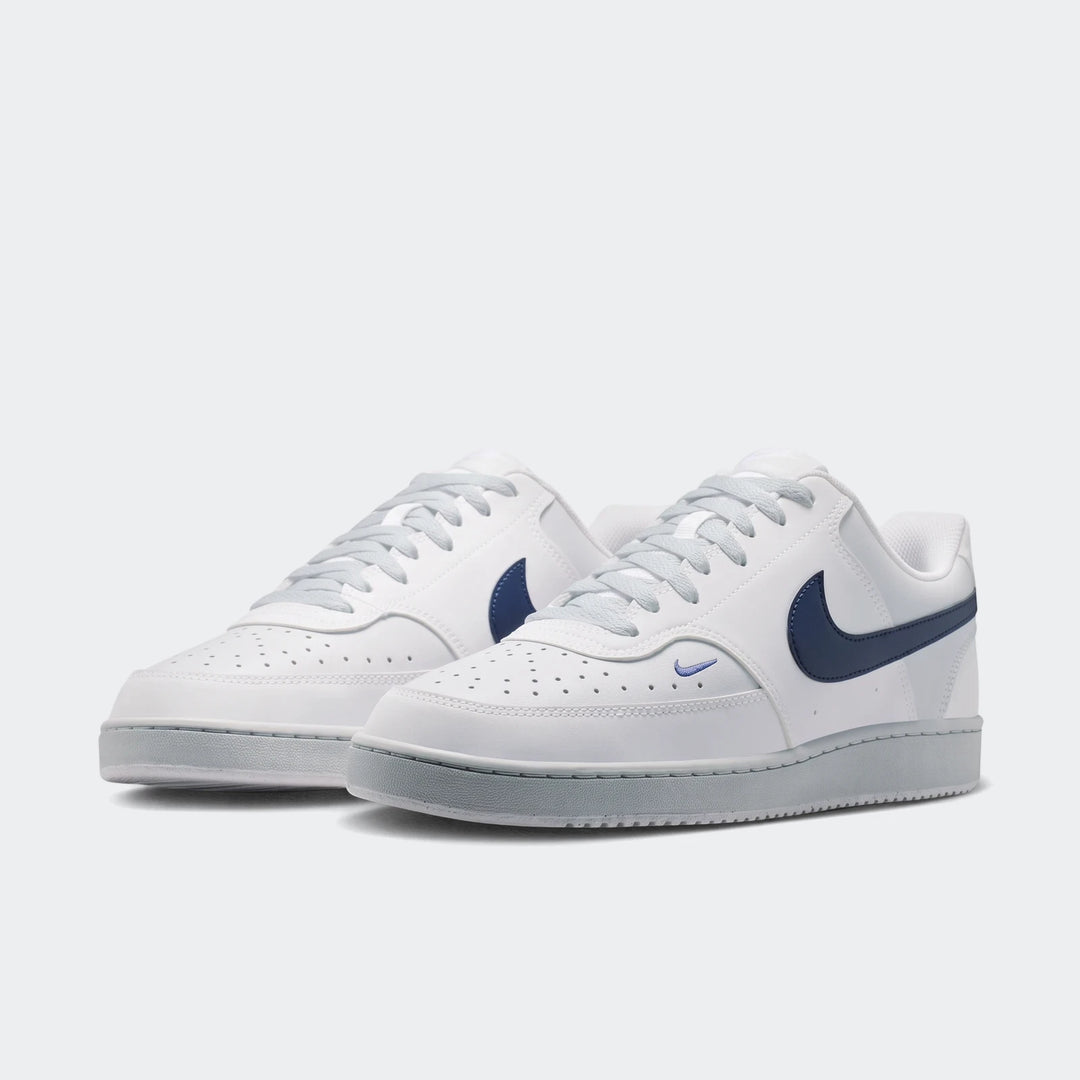 Pair of white Nike Court Vision Low Men's Shoes with navy blue swooshes and light blue laces, viewed from the side.