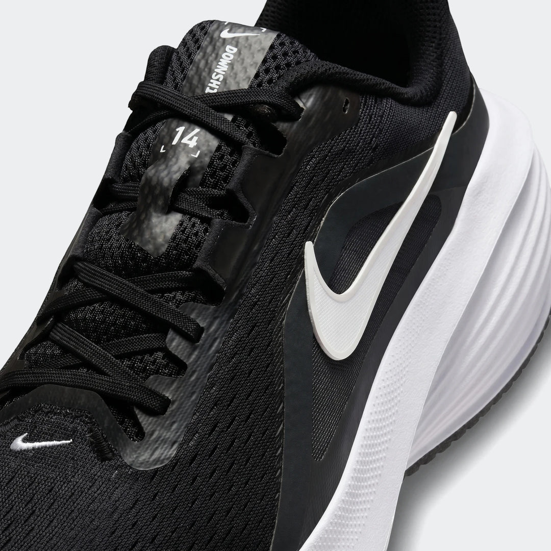 Close-up of a black and white Nike Downshifter 14 men's road running shoe, showcasing its mesh upper, laces, and white