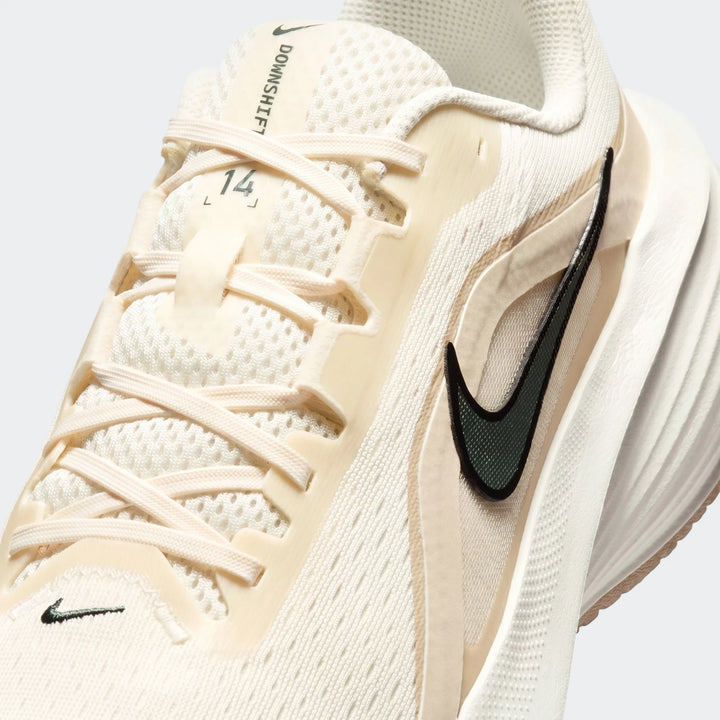 Close-up of a cream and white Nike Downshifter 14 men's road running shoe, highlighting the laces and dark green swoosh.