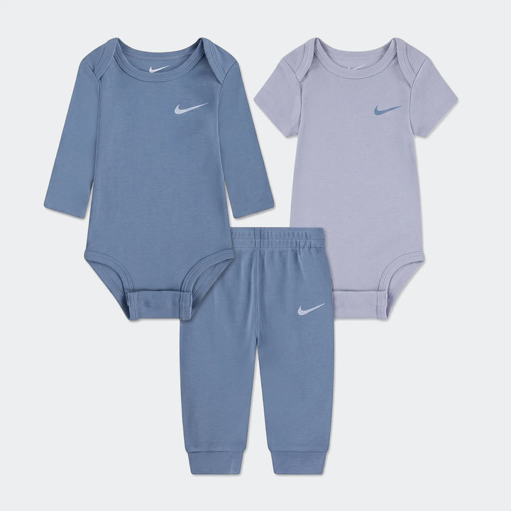 Nike Essentials 3-piece infant set featuring a blue long-sleeve bodysuit, a lavender short-sleeve bodysuit, and blue pants.