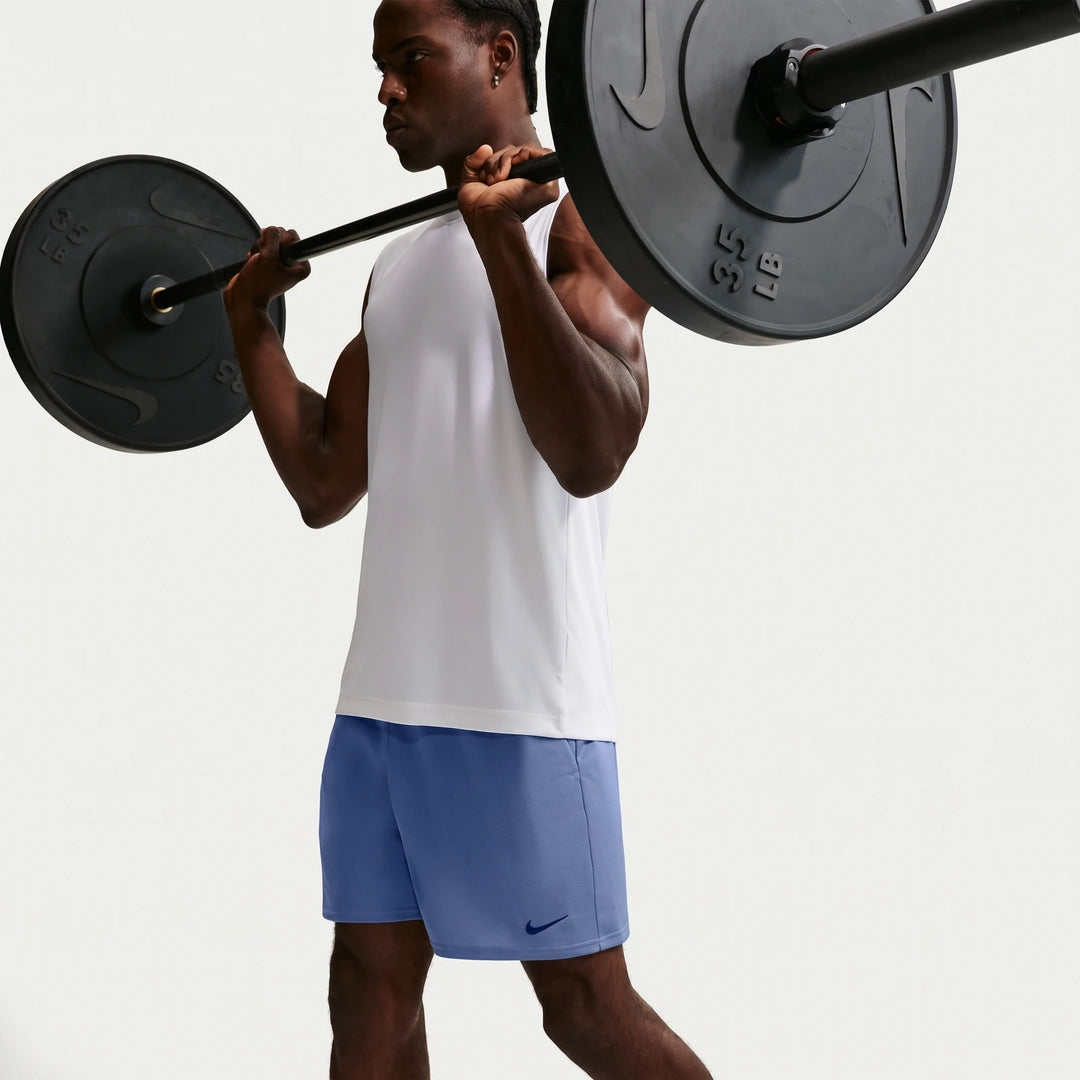 A man in blue Nike Flex Men's Dri-Fit 7" Training Shorts and a white tank top lifting a barbell.