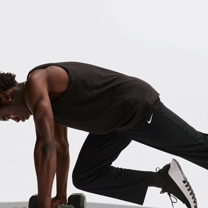 Black Nike Flex Men's Dri-Fit Pants worn by a man performing an exercise with dumbbells in a studio setting.