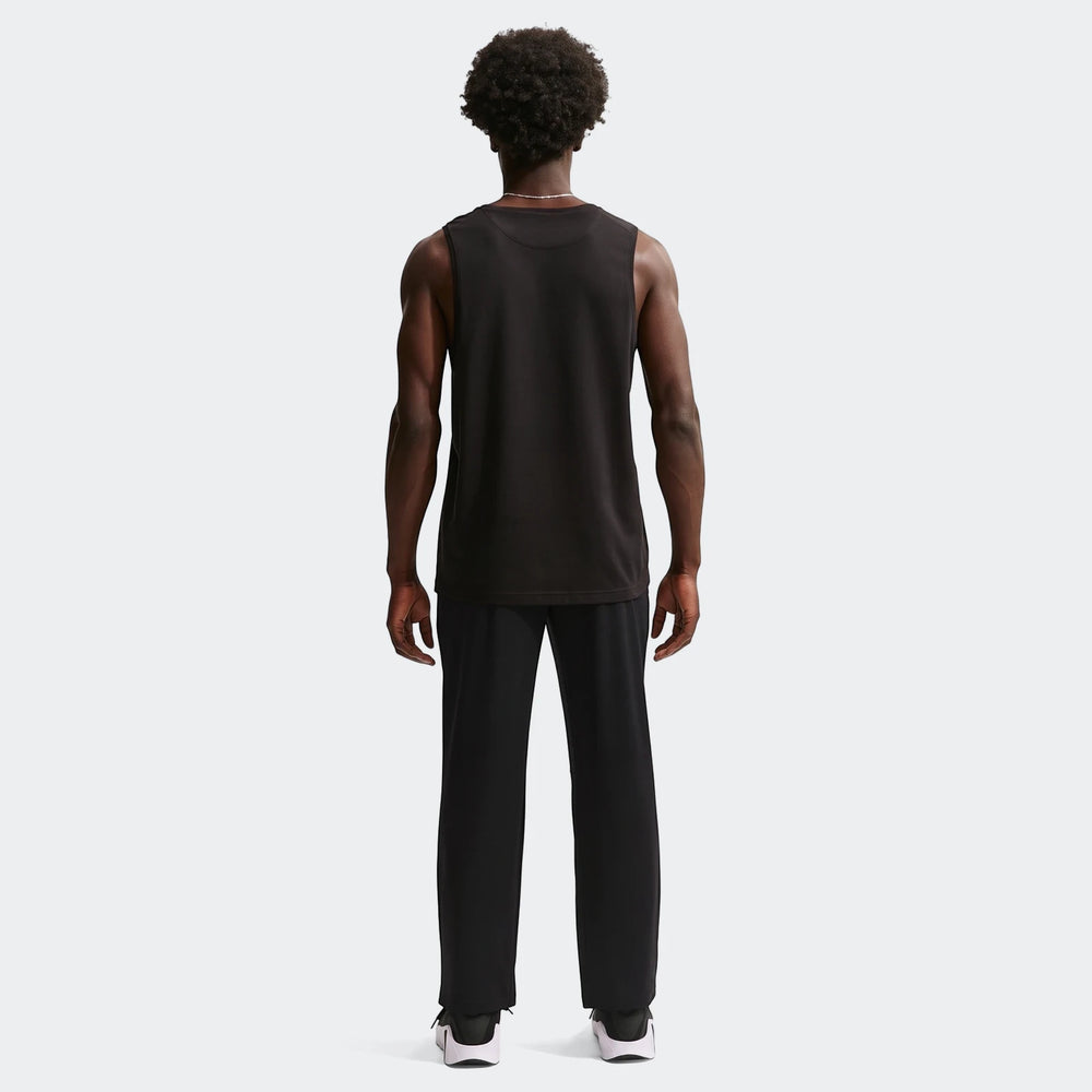 Full body back view of a man wearing black Nike Flex Men's Dri-Fit Pants and a black tank top on a white background.