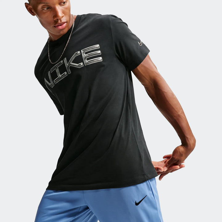 Male model wearing a black Nike t-shirt with silver logo and blue Nike Flex Men's Dri-Fit Pants, posed with hands behind his