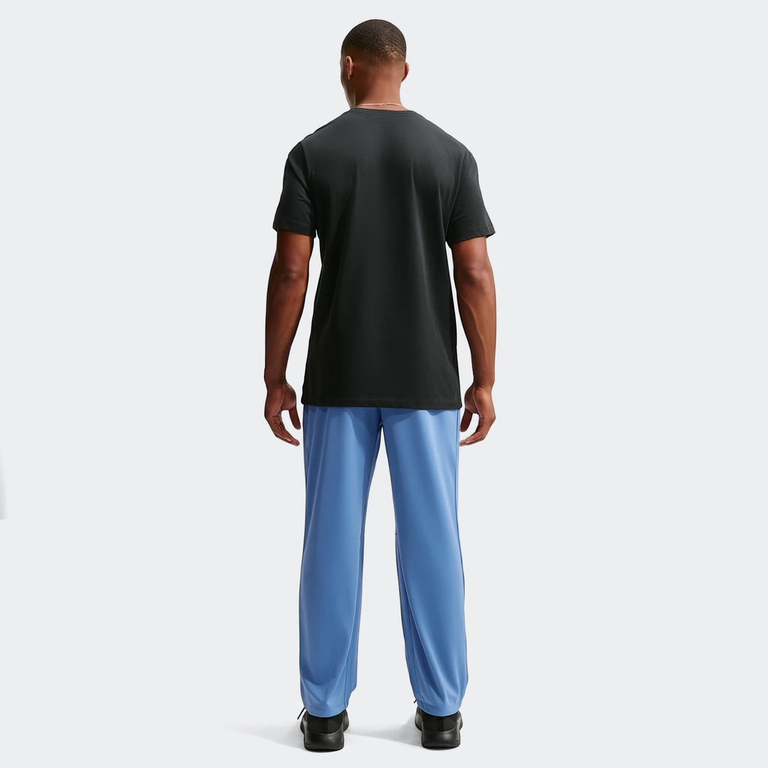 Back view of a man wearing Nike Flex Men's Dri-Fit Pants in blue, paired with a black t-shirt and black athletic shoes.