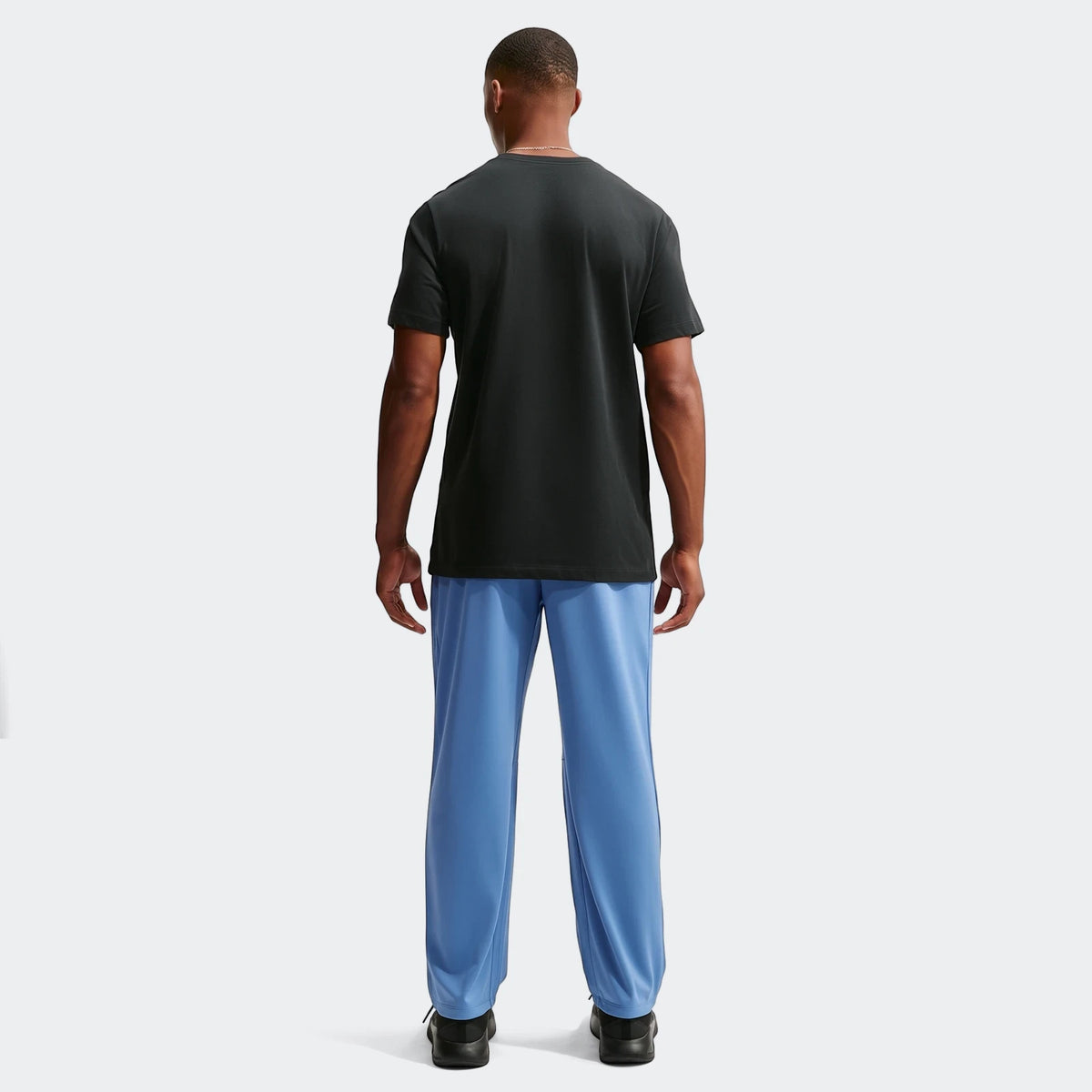 Back view of a man wearing Nike Flex Men's Dri-Fit Pants in blue, paired with a black t-shirt and black athletic shoes.
