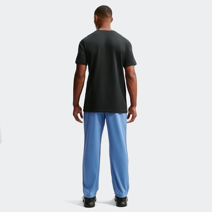 Back view of a man wearing Nike Flex Men's Dri-Fit Pants in blue, paired with a black t-shirt and black athletic shoes.