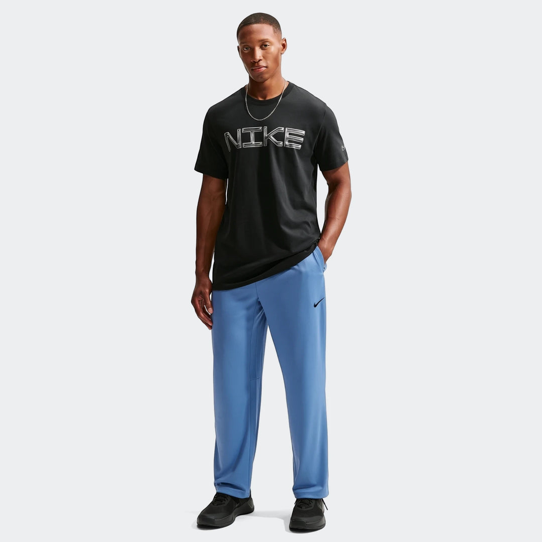 A male model wears Nike Flex Men's Dri-FIT Pants in blue, a black Nike t-shirt, and black sneakers, standing full length.