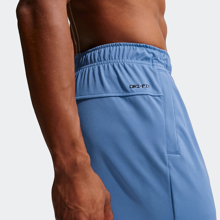 Close-up side view of a man wearing blue Nike Flex Men's Dri-Fit Pants, showcasing the fabric and 'Dri-Fit' logo.