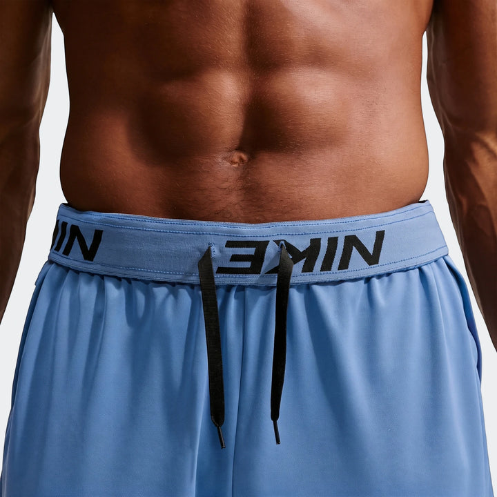 A close-up of a man's torso wearing blue Nike Flex Men's Dri-Fit Pants, featuring the Nike logo waistband and black