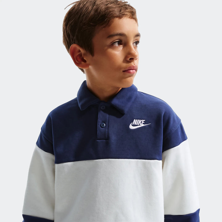 Young boy wearing a navy blue and white Nike K Nsw Club Rugby Ft Lbr long-sleeve polo shirt, looking right.