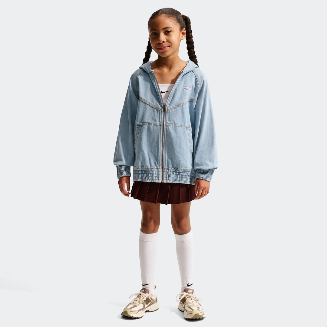 Young girl wearing a light blue Nike denim full-zip jacket, dark red pleated skirt, white socks, and sneakers.