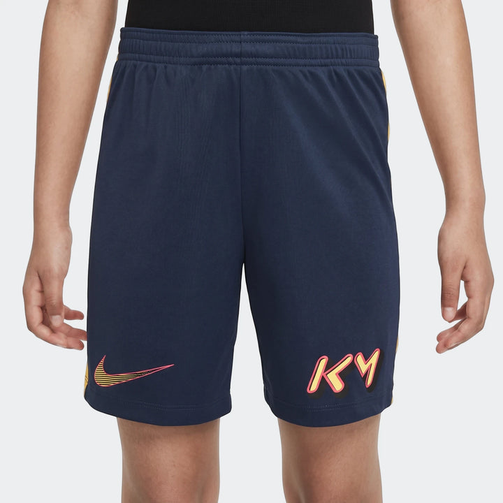 Navy blue Nike Km K Nk Df Acd23 youth athletic shorts with yellow and pink logos, worn by a child from the waist down.