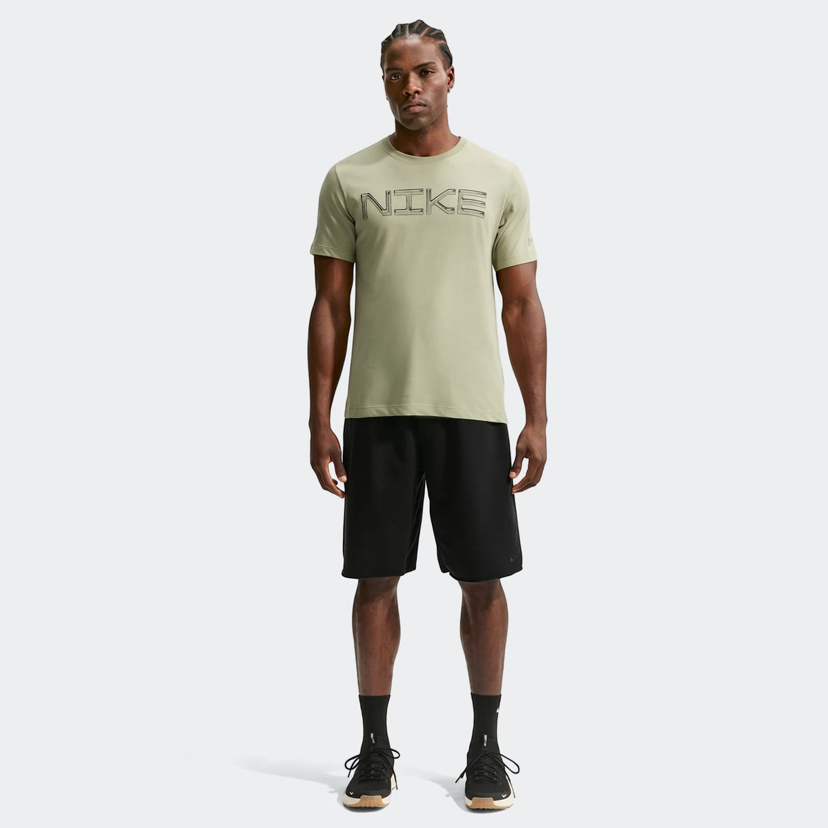 Full body shot of a man wearing a light green Nike Dri-Fit training t-shirt and black shorts, standing on a white background.