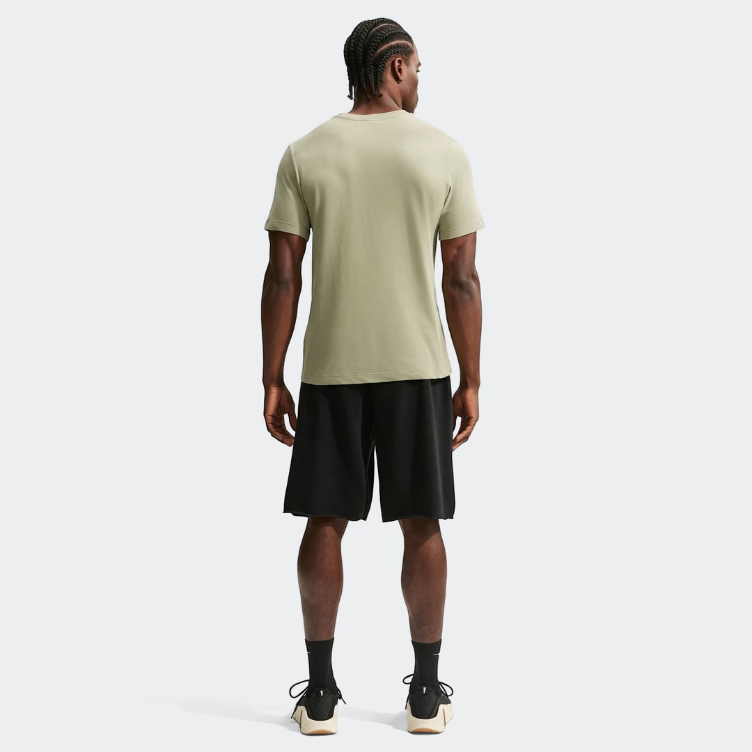Back view of a man wearing a light olive green Nike Men's Dri-Fit Training T-Shirt and black athletic shorts on a plain